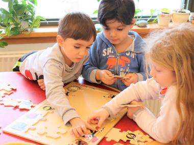 Tre børn samler fælles puslespil med stor koncentration 